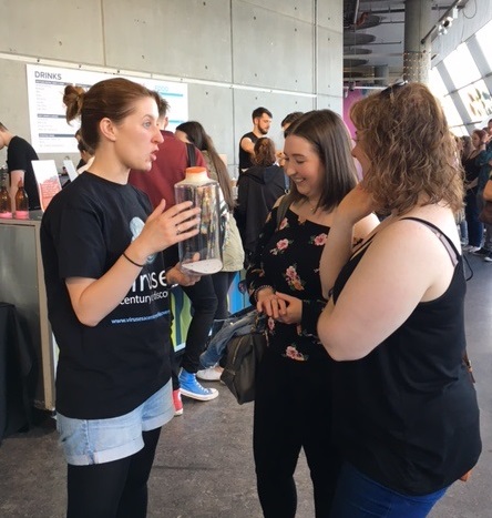 Claire Donald speaks with two female members of the public at Science Lates while holding a sealed container of mosquitoes